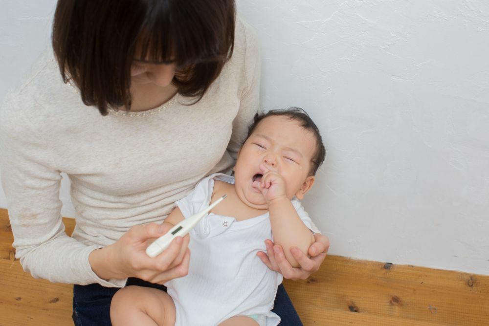 泣いている幼児に母親が体温計を向けている様子